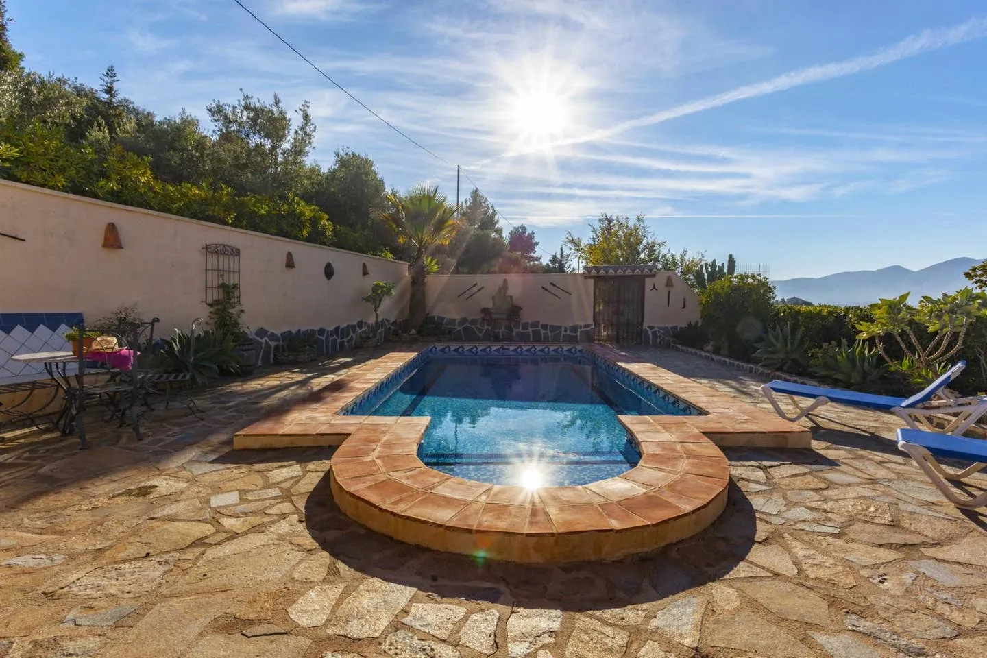 Piscina privada de Villa Loaisa a pleno sol, con solado de piedra natural, tumbonas azules y las montañas de Benissa al fondo
